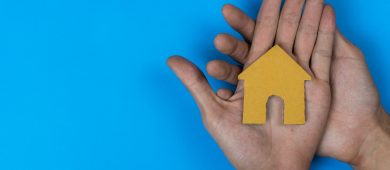 Buy or rent. A small house model made by paper cut on a man hand on  blue background.
